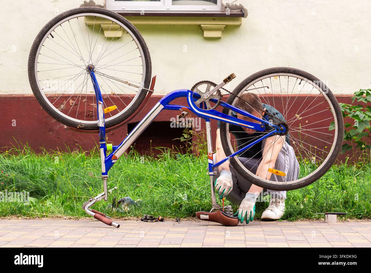 Homme retournant le vélo à l'envers devant la maison. Vérification des roues et de la chaîne pour détecter les dommages. La réparation du vélo montre l'autonomie. Préparation saisonnière pour les balades d'été Banque D'Images
