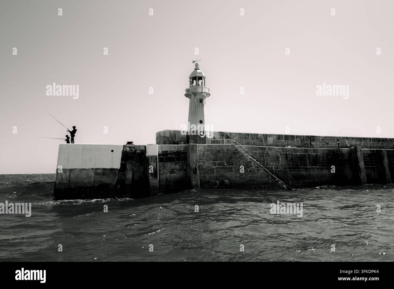 Mur du port de Mevagissy, phare, personnes pêchant à la canne, photographie haute résolution en noir et blanc Banque D'Images