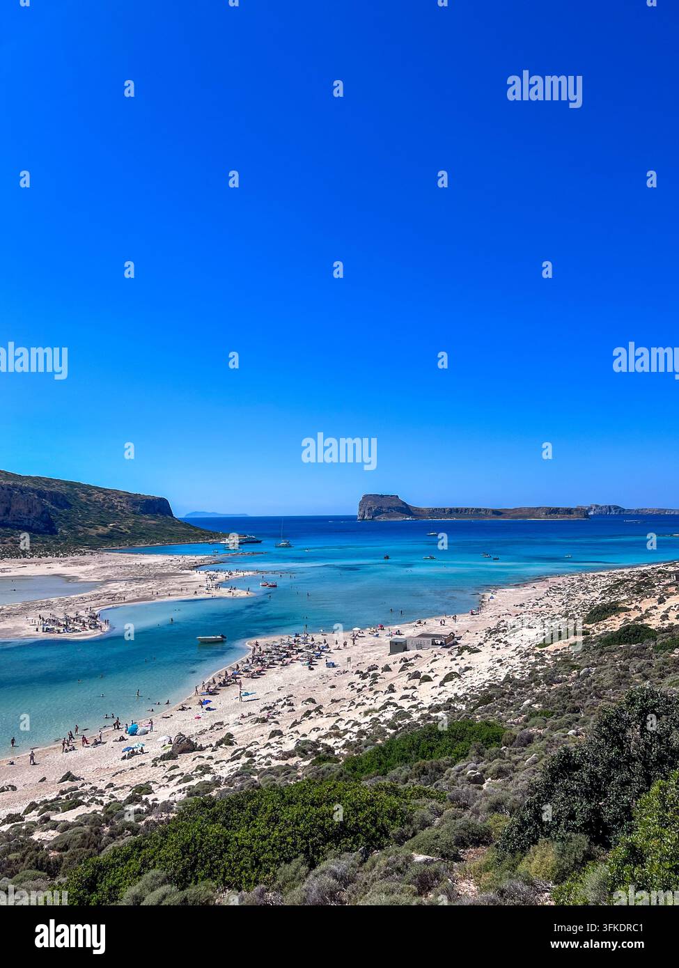 Vue panoramique élevée de la lagune de Balos, Crète, avec des eaux turquoise, une péninsule sablonneuse, des baigneurs et des îlots éloignés. - Image de stock capturée avec un smartphone