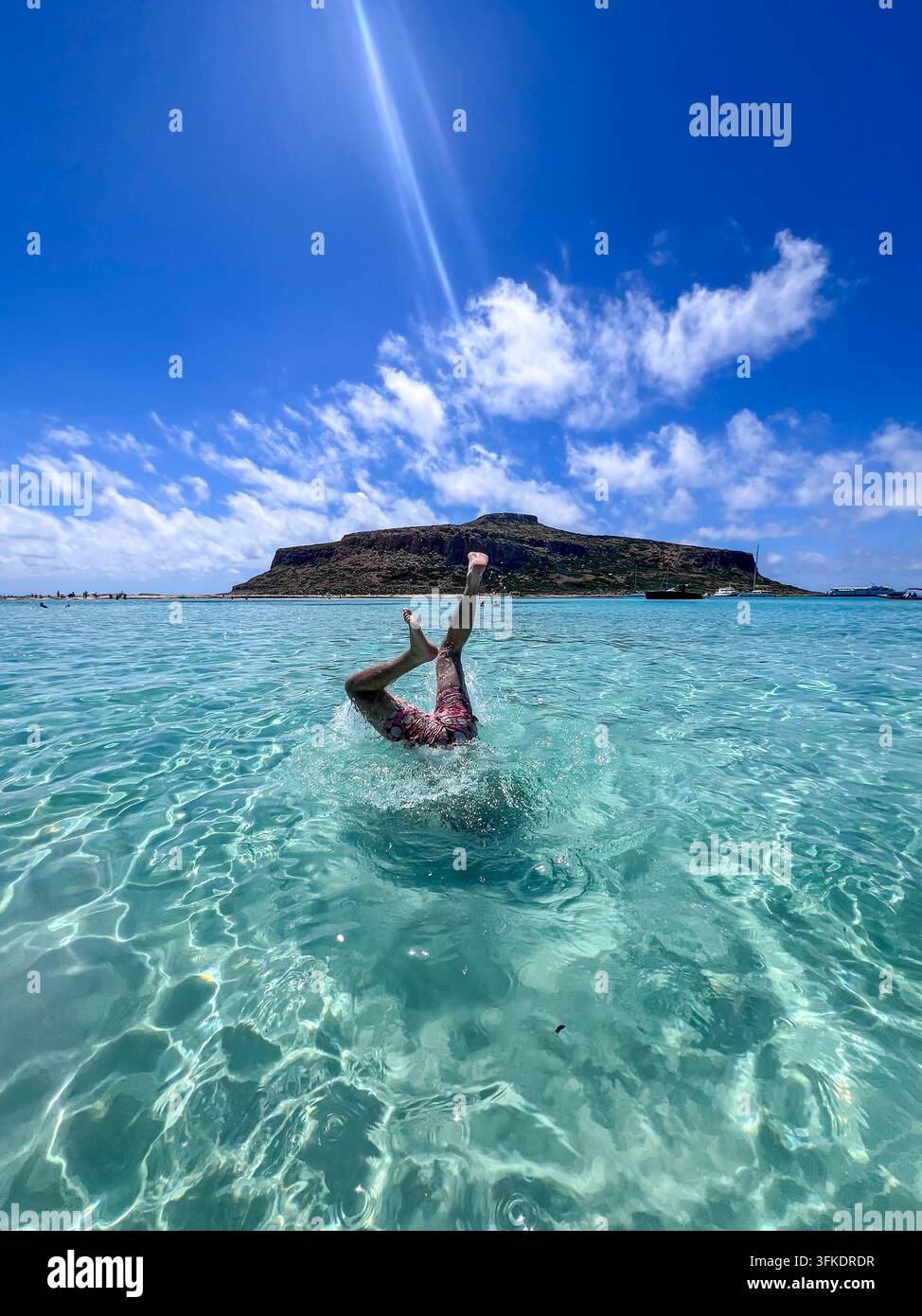 Person plongeant tête la première dans une eau turquoise cristalline à la lagune de Balos, Crète, avec une île rocheuse en arrière-plan. - Image de stock capturée avec un smartphone
