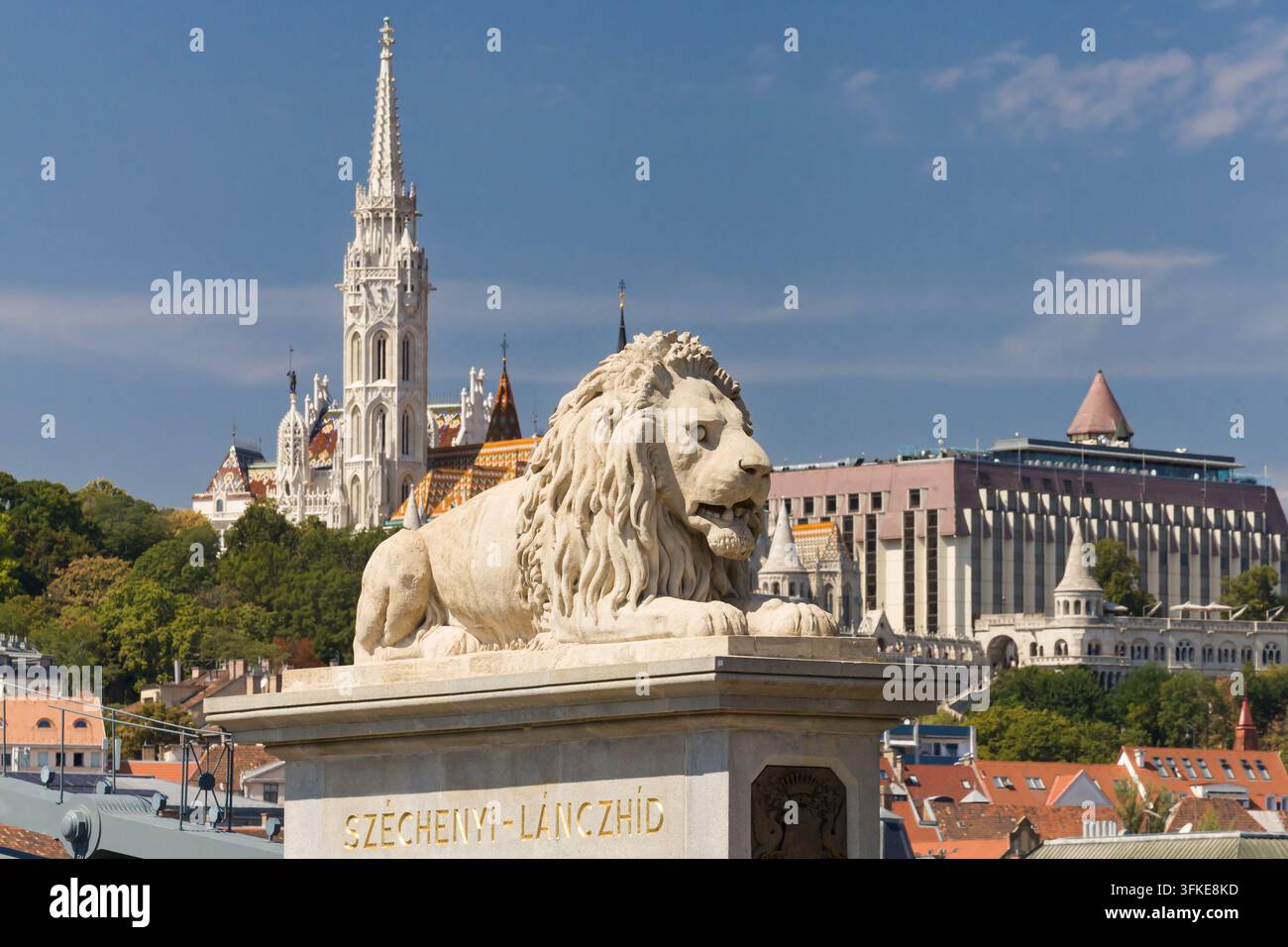 Lion de pierre à l'entrée de Pest du Pont des Chaînes, avec l'église Matthias et la Bastion des pêcheurs au loin à Budapest, Hongrie. Banque D'Images