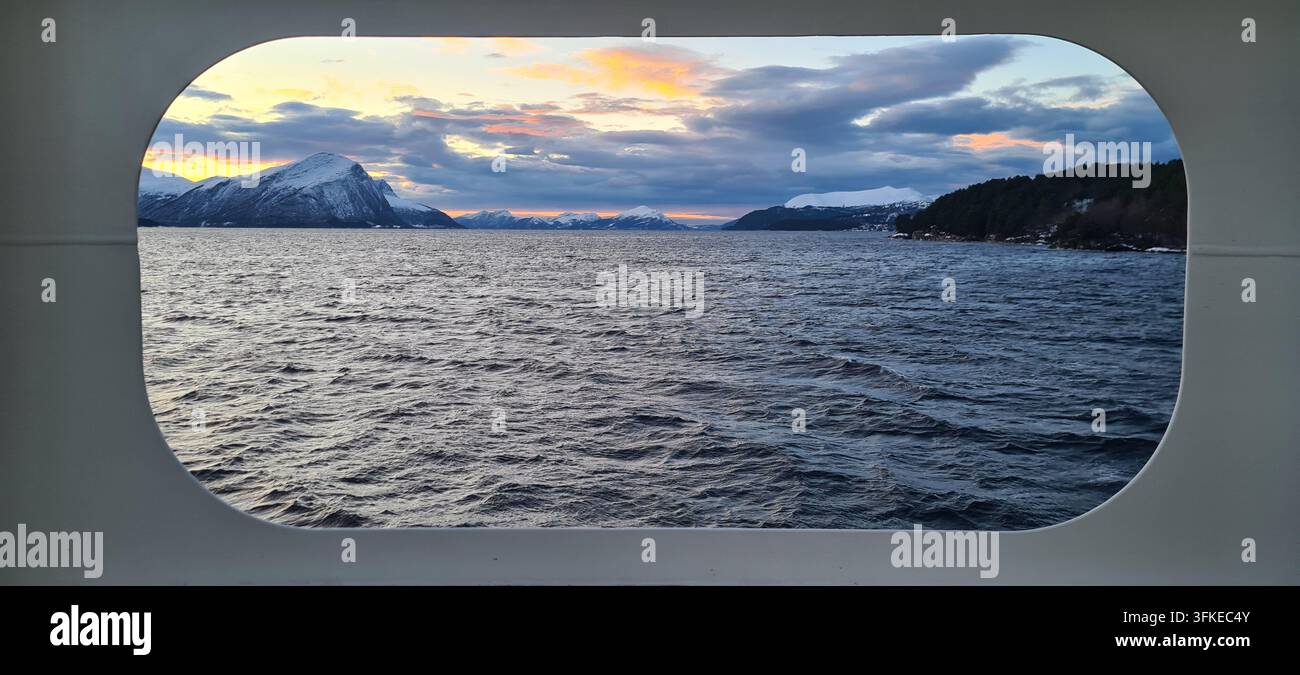 Vue panoramique d'un fjord norvégien et de montagnes enneigées à travers une grande fenêtre à bord d'un navire à passagers, Norvège, avec des nuages dramatiques du soir au-dessus - Image de stock capturée avec un smartphone