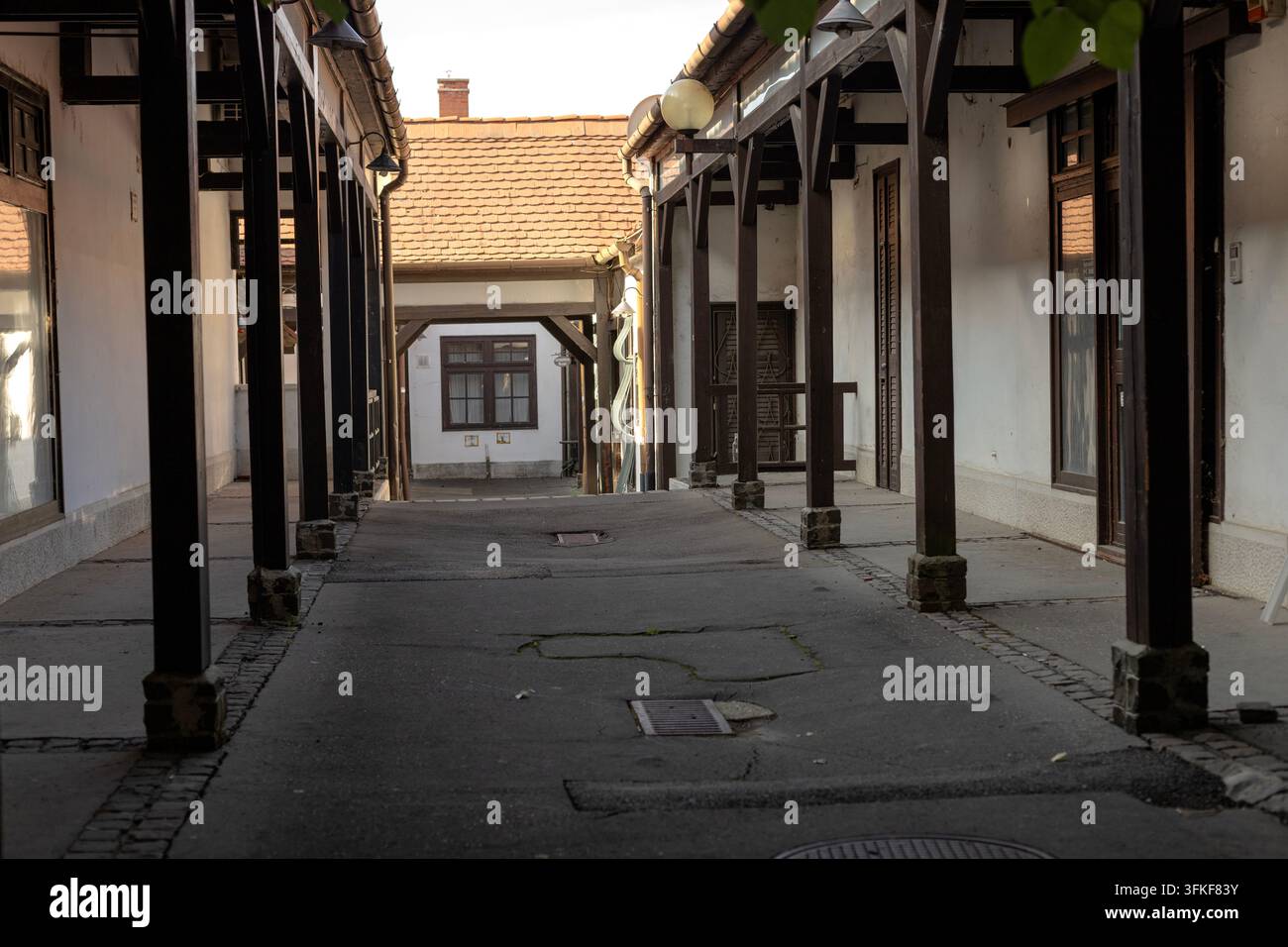 Un passage étroit de cour couvert, bordé de supports en bois, de murs en plâtre blanc, de portes et fenêtres en bois ainsi que de toits carrelés. Une lumière chaude du jour illumine Banque D'Images