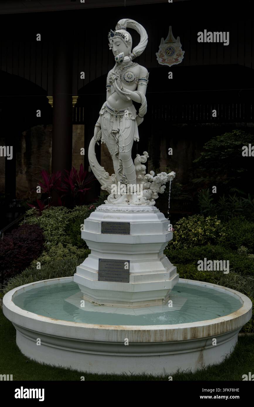 Vue verticale complète de la statue de fontaine en marbre blanc représentant la déesse de la terre Phra Mae Thorani avec un bassin d'eau rond au Wat Phra That Si Mueang sacré Banque D'Images