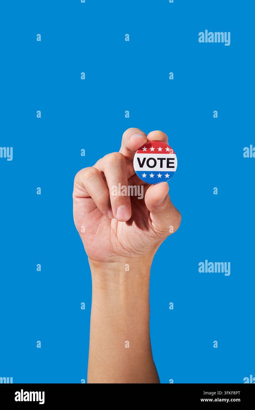 Un homme tient un badge de vote rouge, blanc et bleu entre ses doigts sur un fond bleu vif, avec la main levée et l'avant-bras entourés de gènes Banque D'Images