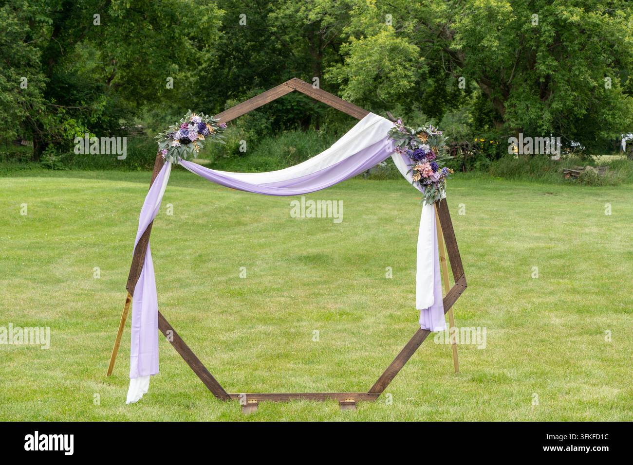 Arche de mariage en bois hexagonale décorée de tissu et de fleurs violettes dans un jardin verdoyant Banque D'Images