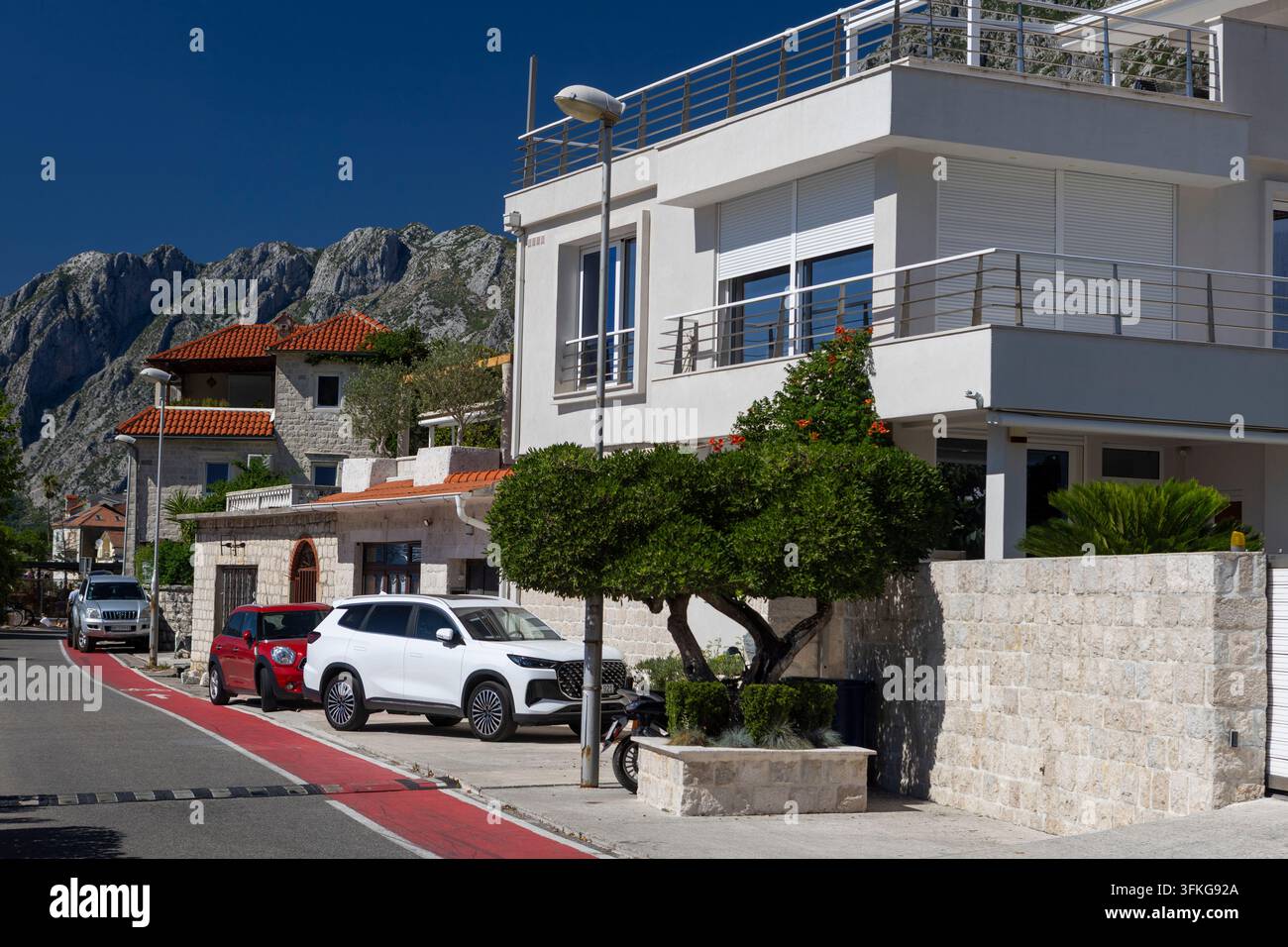 4 juillet 2026, Kotor, Monténégro, Extérieur d'une villa côtière blanche à deux étages avec des rampes de balcon en verre, des tuiles de toit en terre cuite et une limite en pierre Banque D'Images