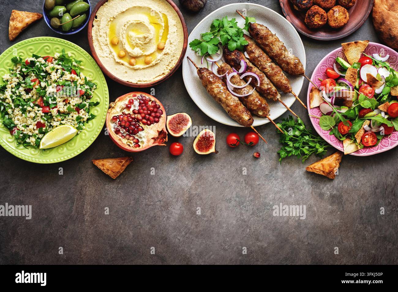 Plats variés du Moyen-Orient et arabes sur un fond rustique sombre. Houmous, taboulé, salade Fattoush, pita, kebab de viande, falafel, baklava, grenade. Nourriture halal. Vue de dessus, flat lay, espace de copie. Banque D'Images