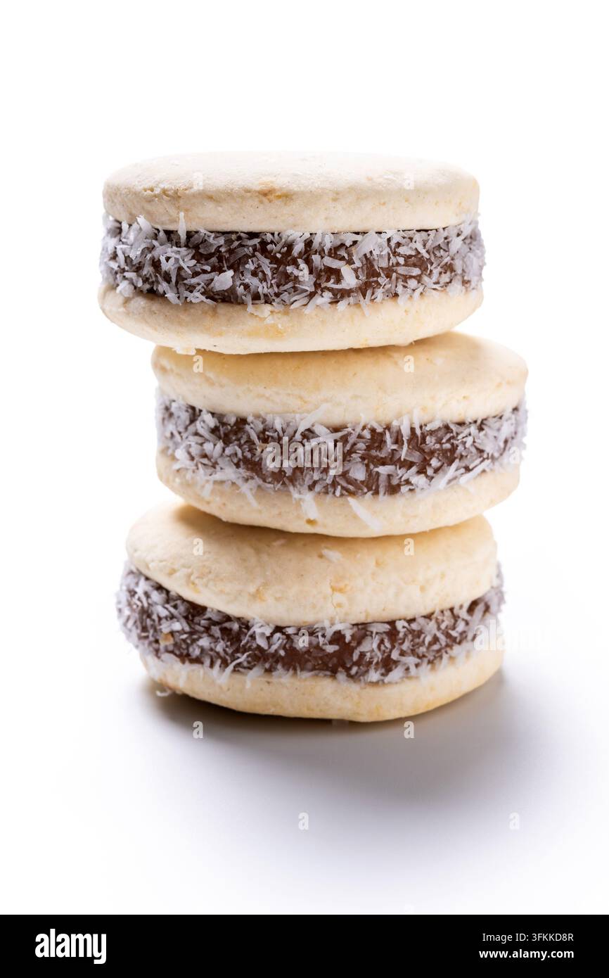 Pile d'alfajores traditionnels faits de biscuits moelleux, fourrés au dulce de leche et recouverts de noix de coco râpée, isolés sur un fond blanc. Banque D'Images