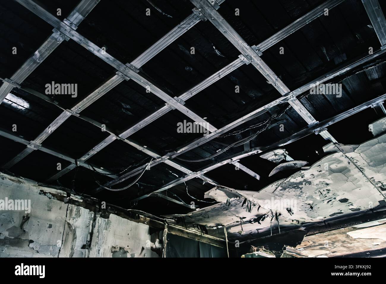 Une pièce intérieure montre un plafond fortement endommagé par le feu avec une grille métallique exposée, des panneaux manquants et des traces de carbonisation et de fumée visibles, destruction Banque D'Images