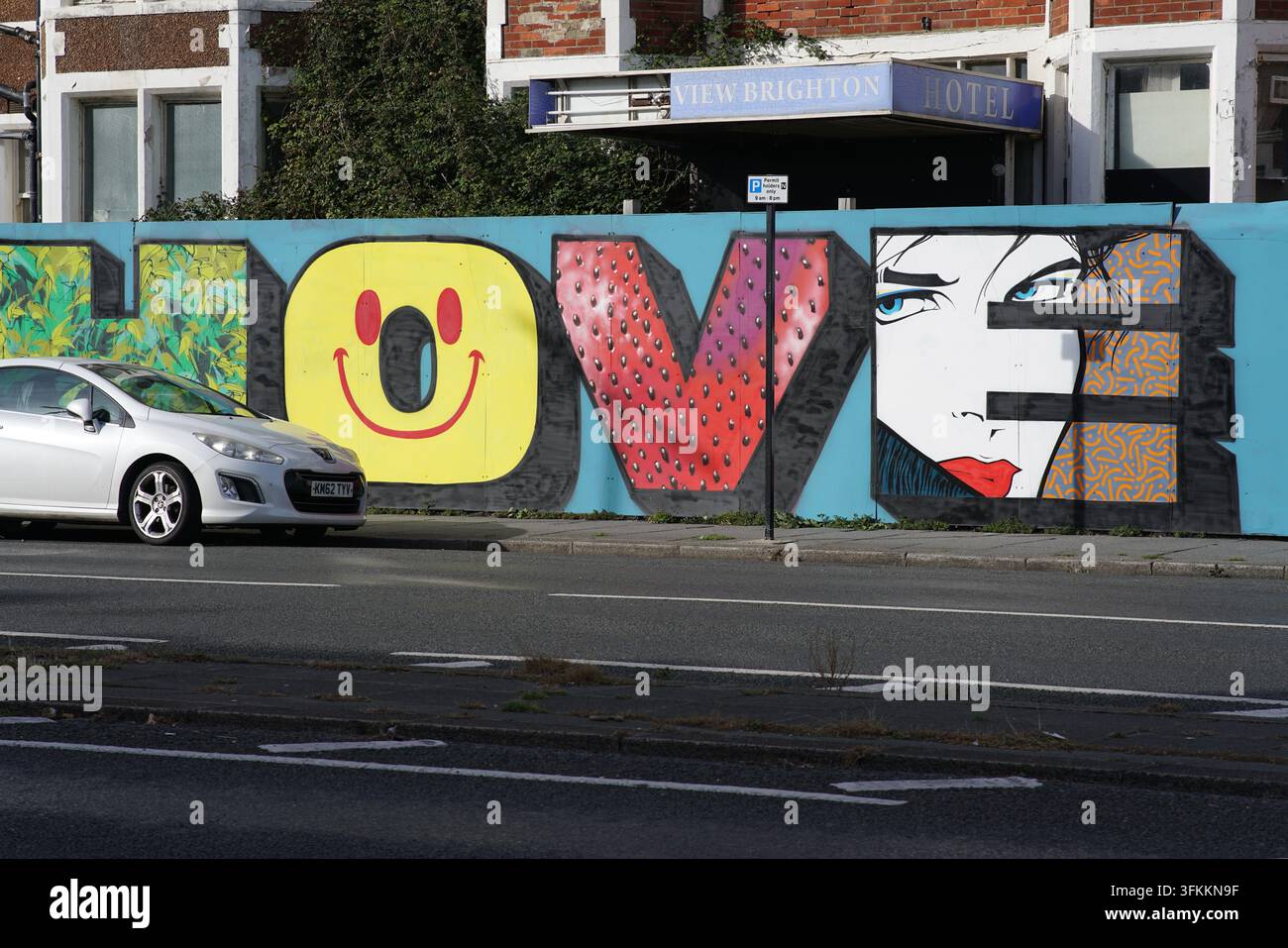 Peinture murale de Hove avec un visage souriant et un portrait à côté d'une voiture qui passe à Hove, Brighton, Angleterre. Banque D'Images