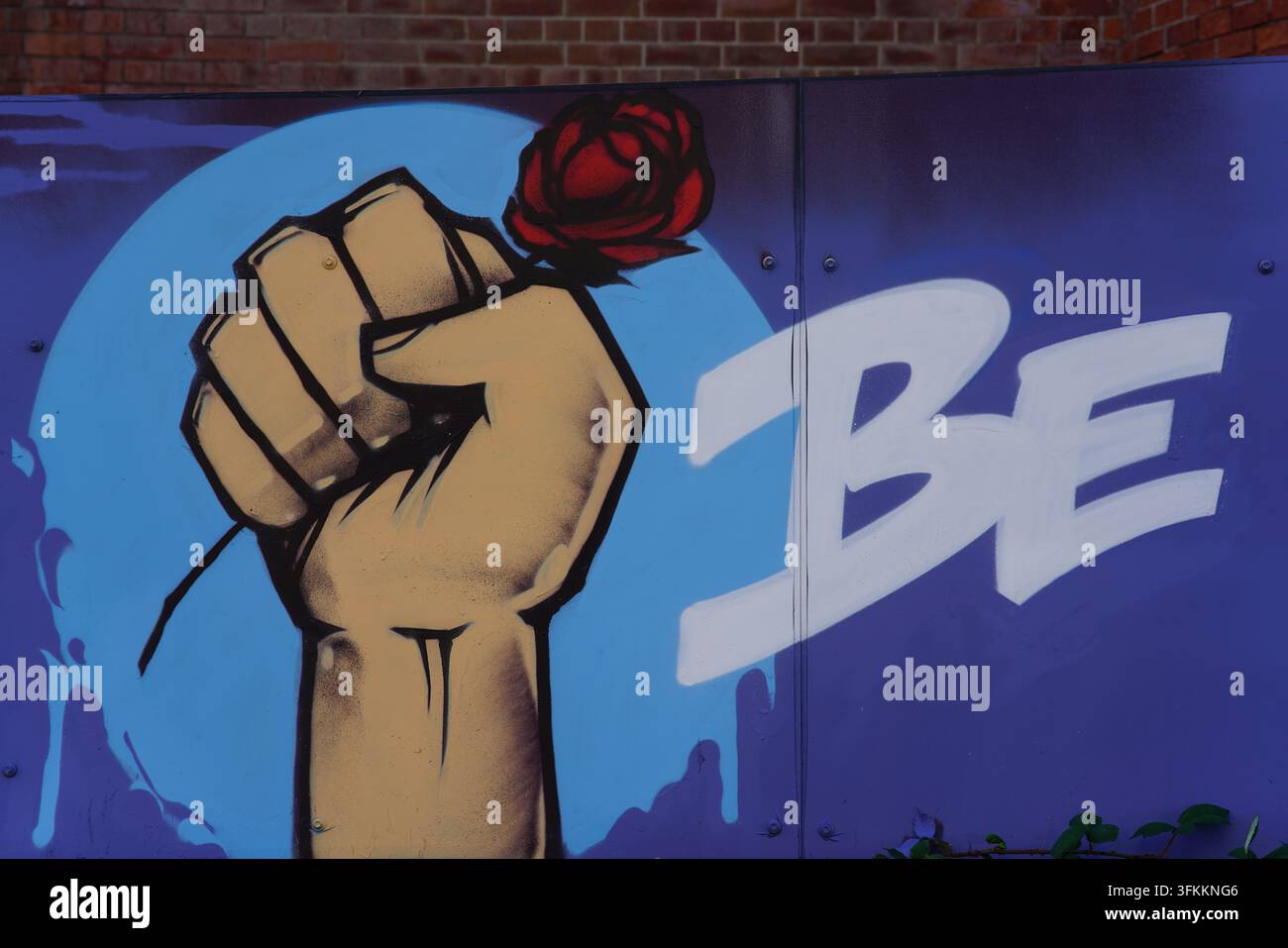 Peinture murale de rue représentant un poing levé tenant une rose rouge à côté des lettres BE à Hove, Brighton, Angleterre. Banque D'Images