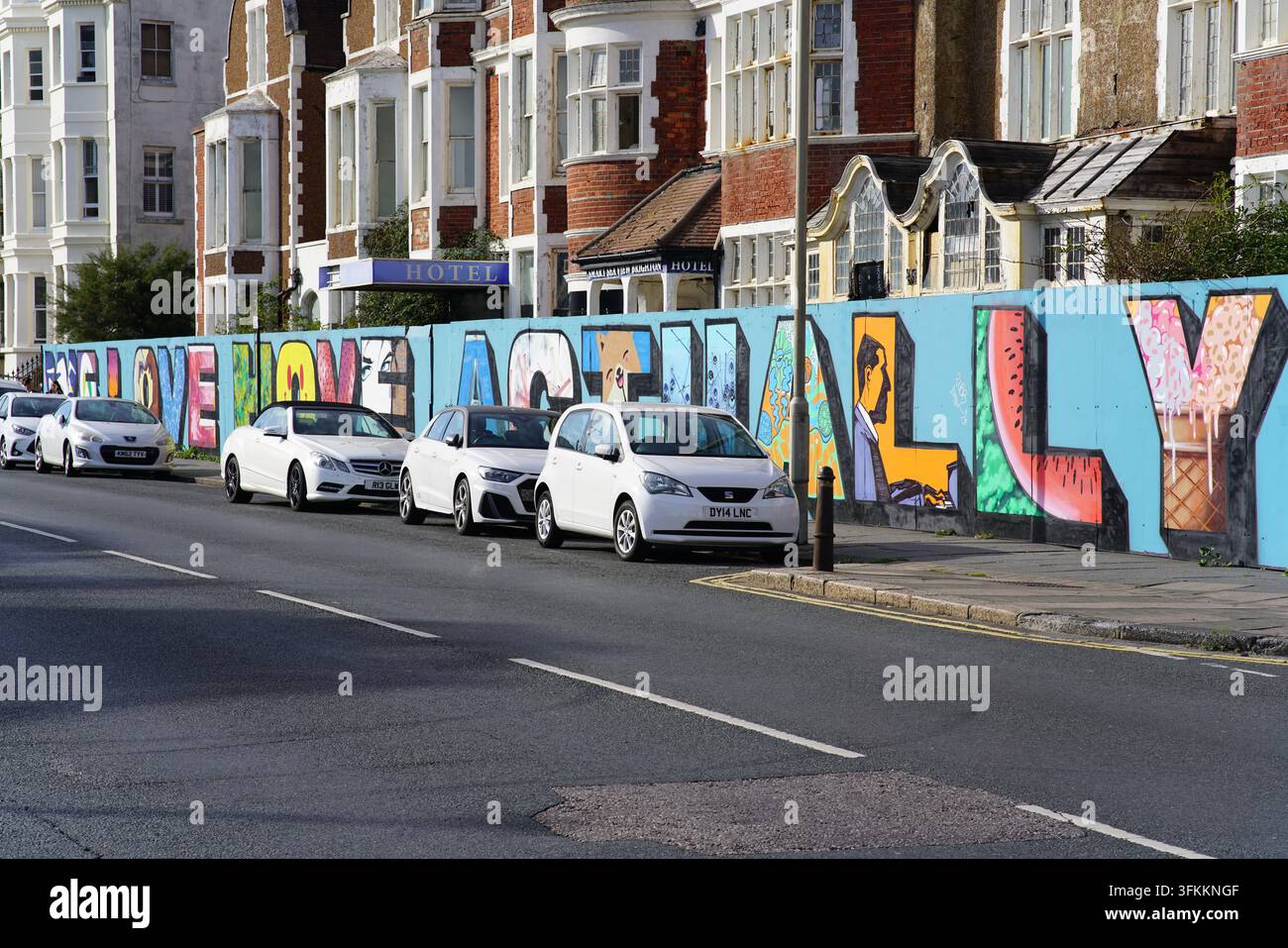 Voitures garées le long d'un mur de graffitis aux lettres colorées dans une rue résidentielle à Hove, Brighton, Angleterre. Banque D'Images
