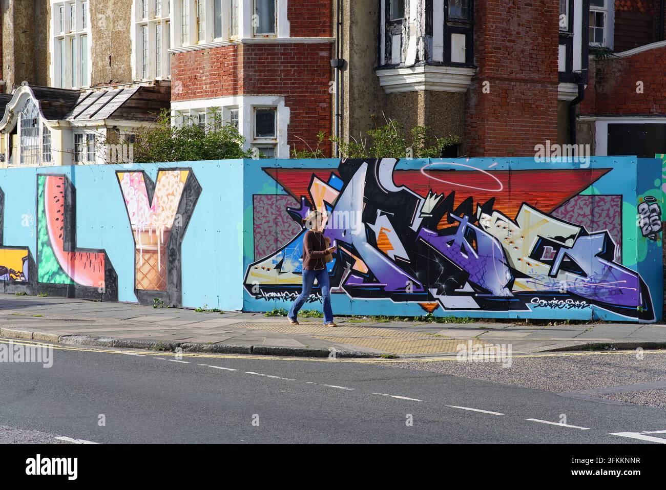 Piéton passant devant une fresque graffiti colorée sur un mur de rue à Hove à Brighton, en Angleterre. Banque D'Images