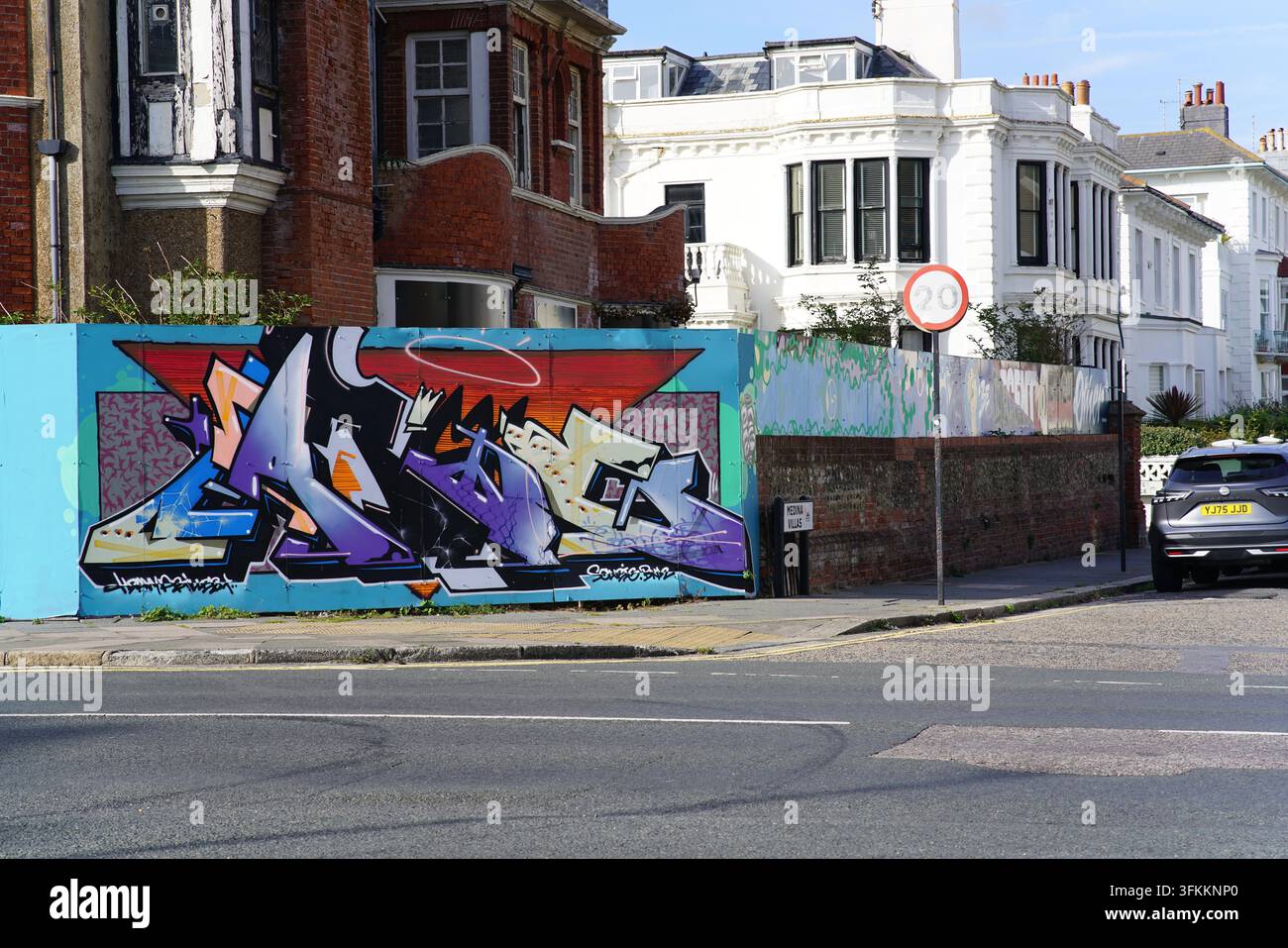 Peinture murale graffiti colorée sur un mur bas devant des maisons en rangée sur une rue ensoleillée à Hove, Brighton, Angleterre. Banque D'Images