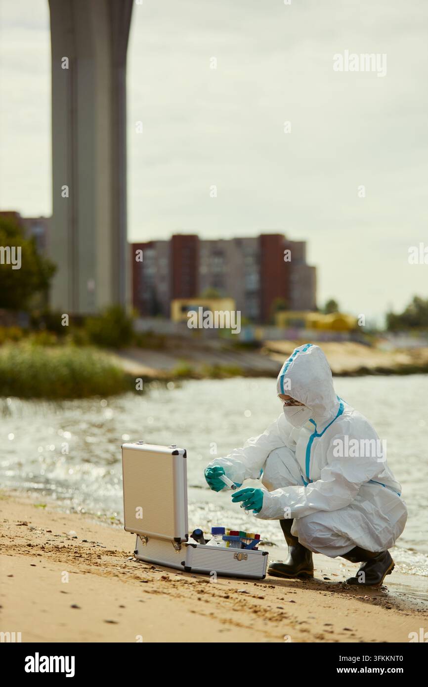 Scientifique féminine en combinaison de protection testant la pollution de l'eau de la rivière Banque D'Images