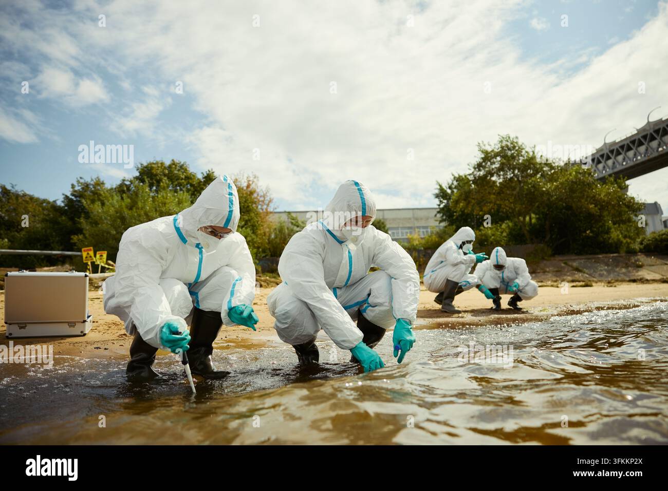 Écologistes en combinaisons de protection échantillonnant l'eau de la rivière sur la rive Banque D'Images