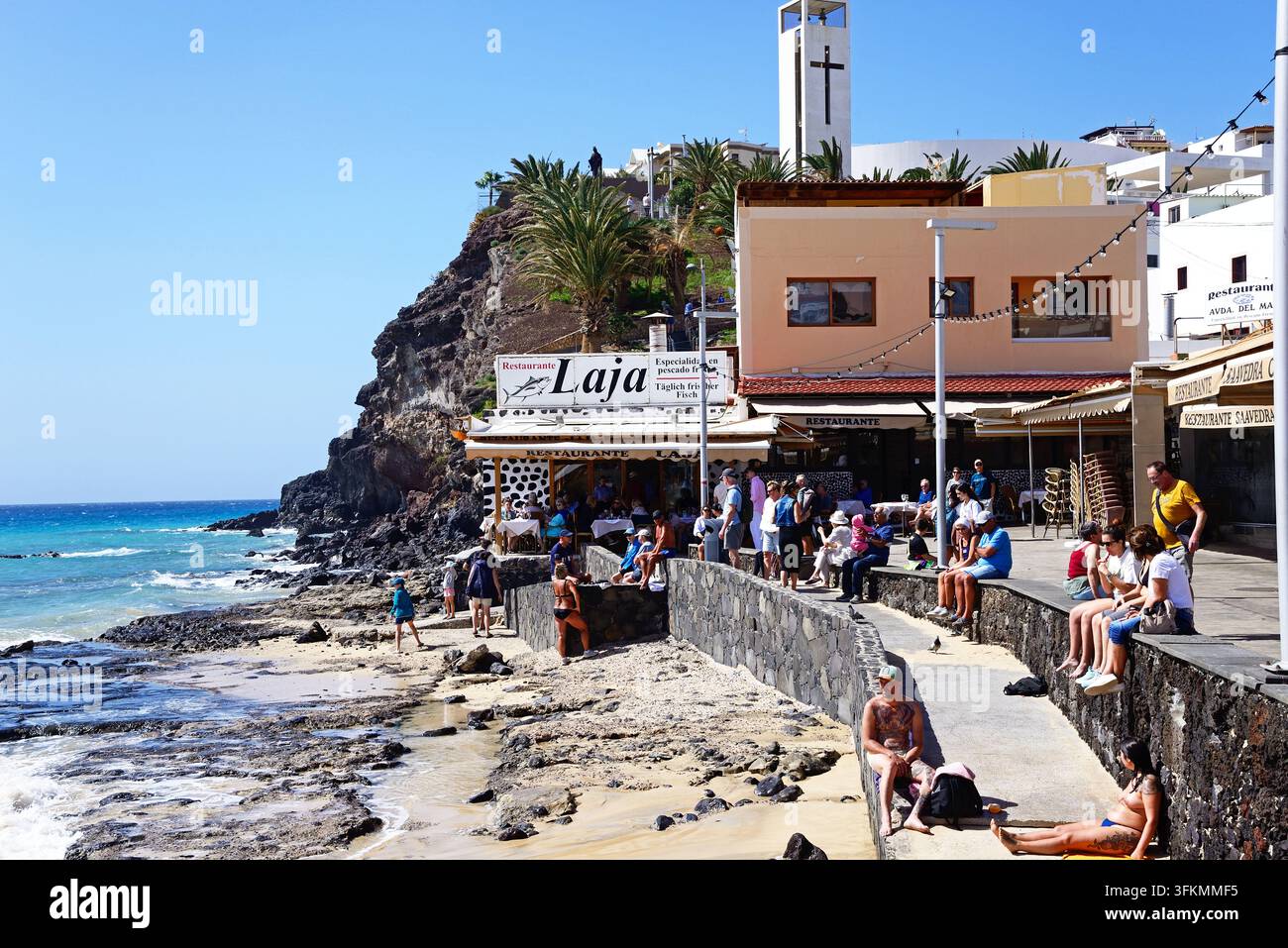 Touristes se détendant le long de la promenade avec des bars et des restaurants à l'arrière-plan et une vue sur la mer, Morro Jable, Fuerteventura. Banque D'Images