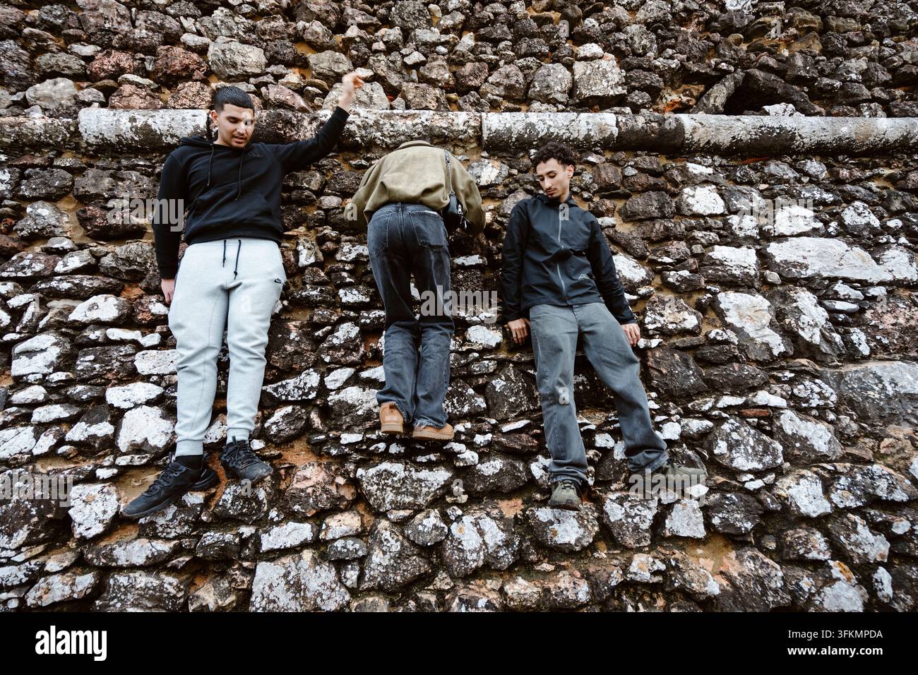 Nazare, Portugal - 6 décembre 2025 : Trois jeunes hommes debout sur les rochers à Nazare, au Portugal. Banque D'Images
