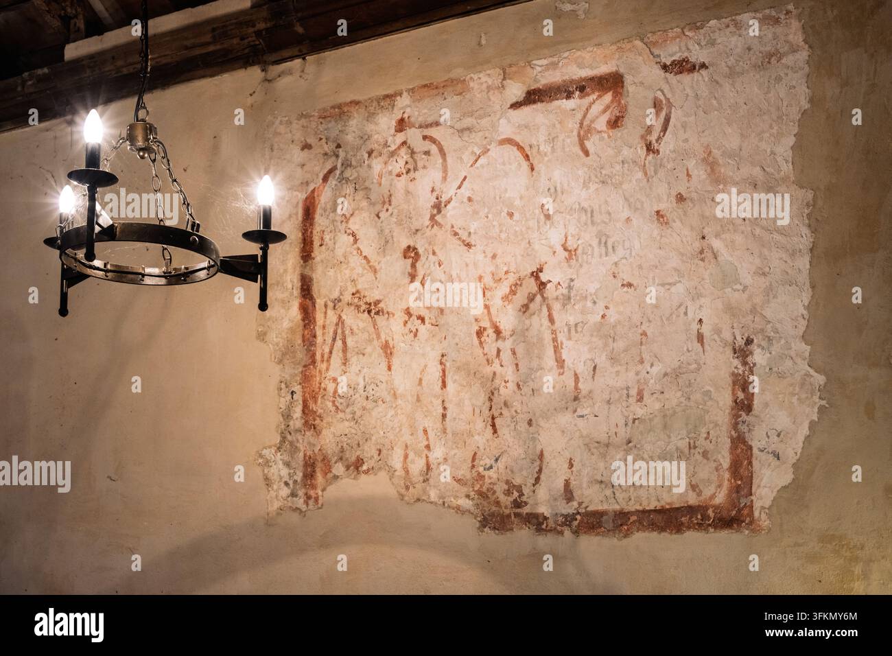 Un fragment de peinture murale médiévale décoloré illuminé par un lustre à anneaux en métal à l'intérieur de l'église classée Grade I de St Giles dans la ville fantôme d'Imber, Royaume-Uni Banque D'Images