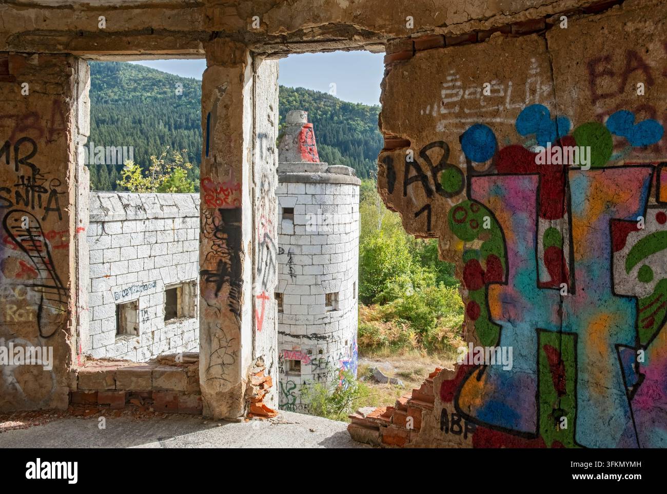 Vue à travers une fenêtre brisée de Bistrik Kula montrant les ruines d'une tour en pierre couvertes de graffitis sur le mont Trebević à Sarajevo, Bosnie-Herzégovine Banque D'Images