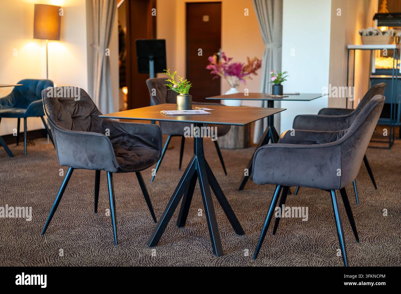 Petites tables entourées de confortables fauteuils recouverts de daim dans un intérieur de café chaleureux, préparés et attendant les invités. Banque D'Images