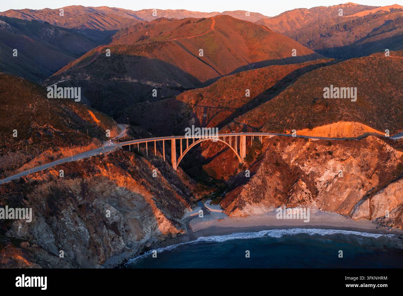 Vue aérienne capturant le pont de Bixby Creek le long de la Pacific Coast Highway à Big Sur, en Californie, enjambant un canyon côtier rocheux sous la lumière chaude du coucher de soleil Banque D'Images