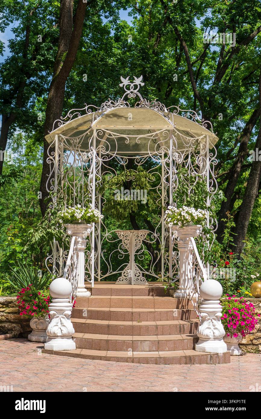 Gazebo en métal blanc d'extérieur avec toit dans un jardin devant des arbres verts. Lieu de détente et d'intimité Banque D'Images