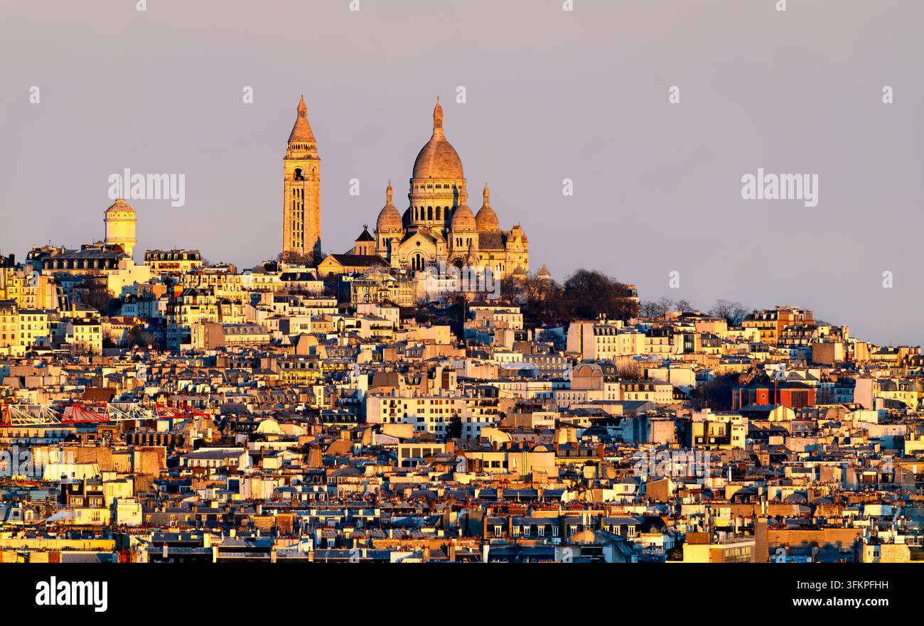 Vue panoramique élevée de la basilique du Sacré-Cœur et de la colline de Montmartre entourée de bâtiments parisiens denses au coucher du soleil à Paris, France. Banque D'Images