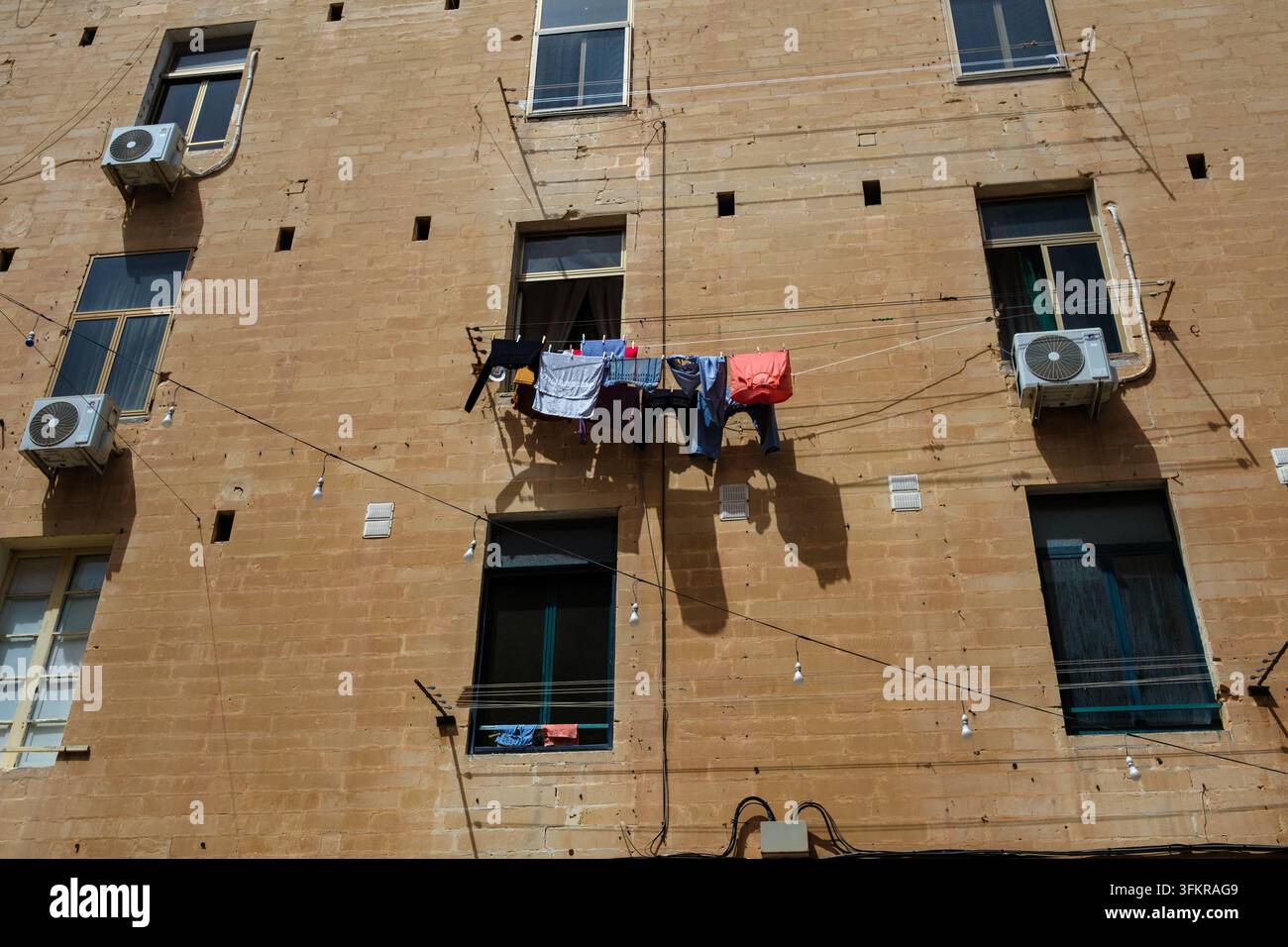 Vêtements lavés séchant accrochés à l'extérieur des fenêtres sur des cordes à linge sous le soleil chaud à La Valette, Malte, contrastant avec le calcaire Banque D'Images