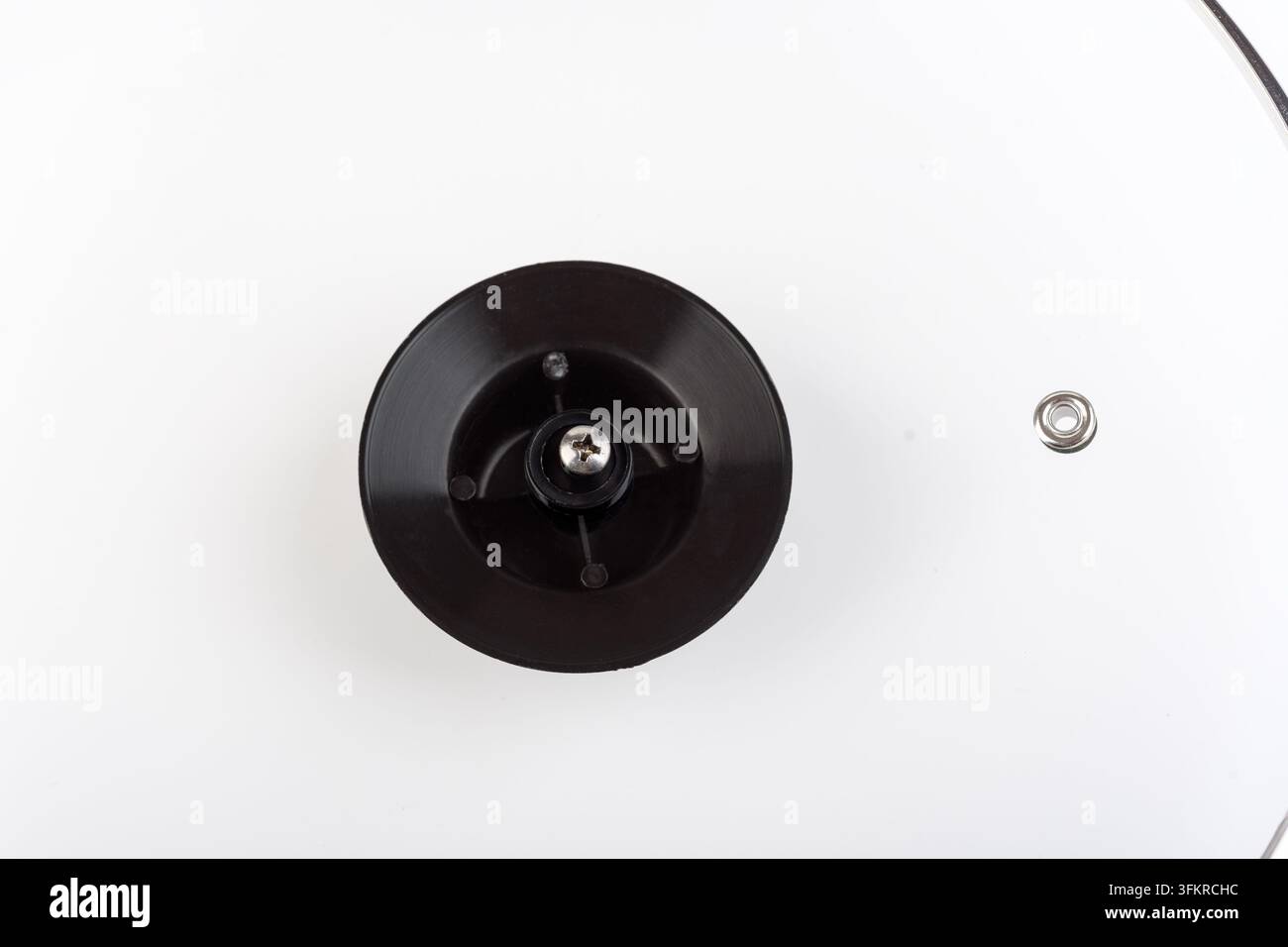 Une photographie macro en studio détaillée, se concentrant étroitement sur la base d'un bouton de couvercle de pot noir et circulaire. Une seule vis à tête cruciforme est partiellement insérée Banque D'Images