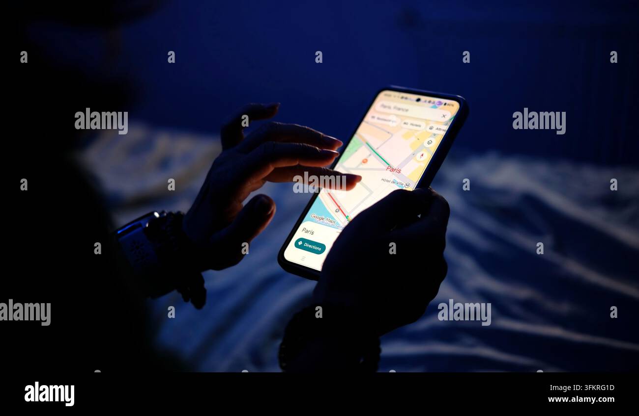 Paris, France – 25 octobre 2025 : Une fille parcourt Google Maps sur son smartphone à la maison la nuit, explorant les rues et les sites touristiques de Paris au lit Banque D'Images