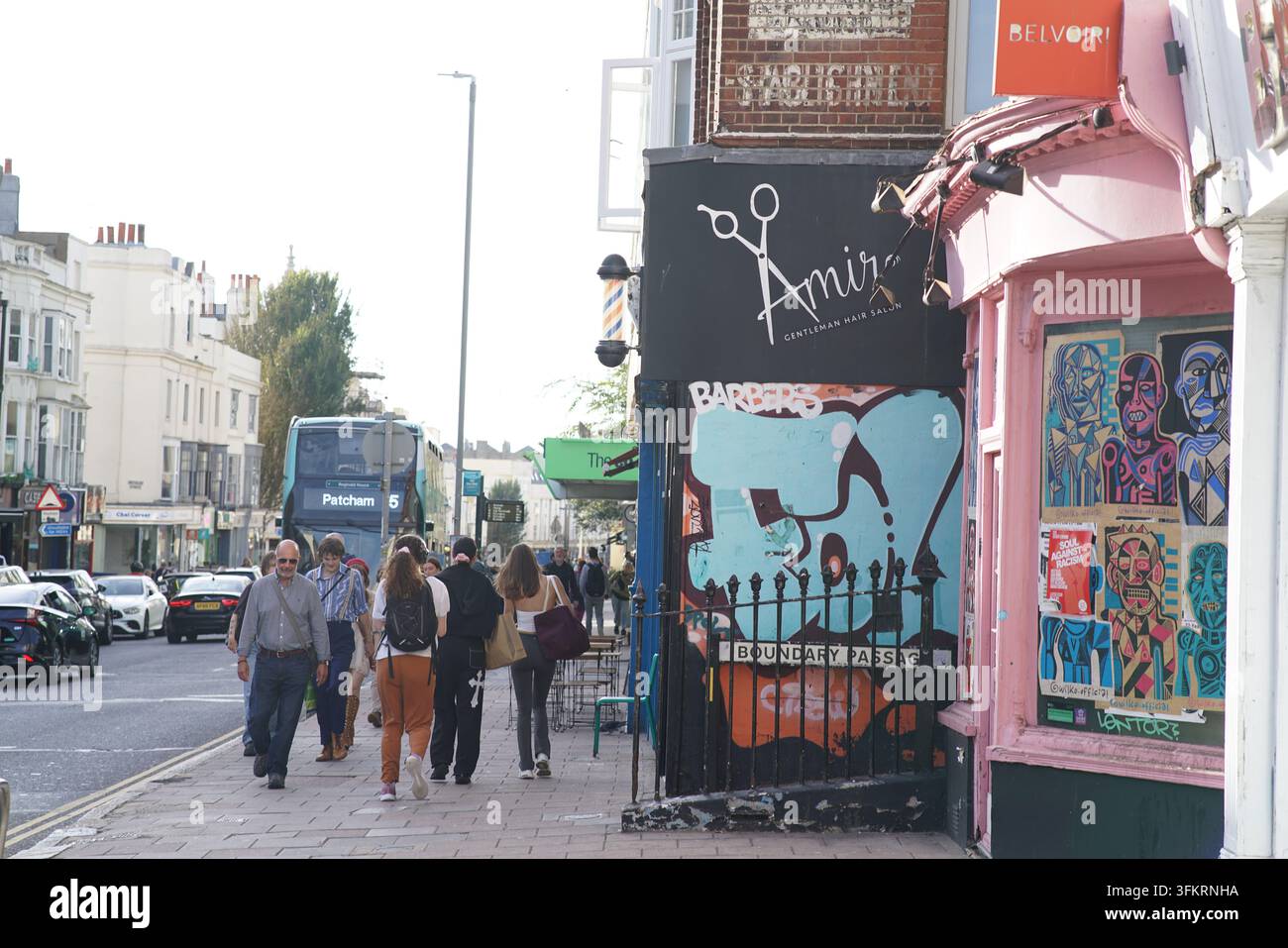 Des piétons passant devant un salon de coiffure, une porte graffiti et une boutique rose dans une rue de Brighton, en Angleterre. Banque D'Images
