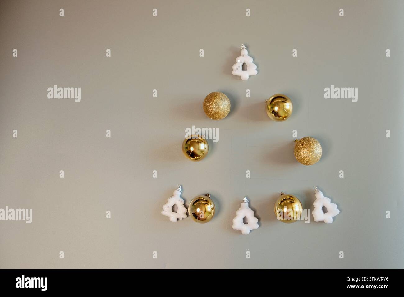 Arrangement minimaliste de petites boules de Noël dorées et d'ornements de flocons de neige blancs sur un fond neutre, adapté à un design de fêtes épuré Banque D'Images