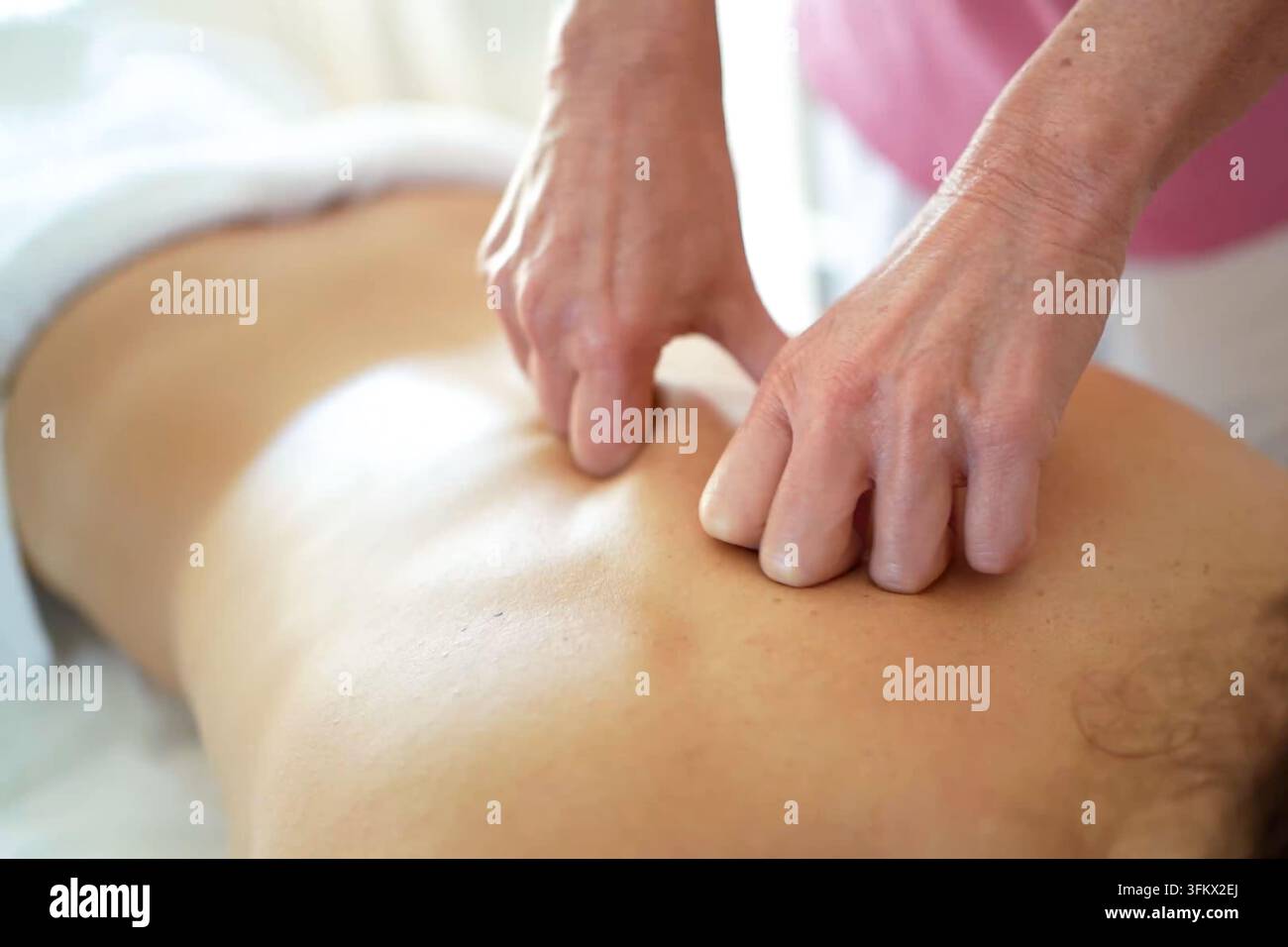 Séance de massage avec des mains massant le dos dans un environnement détendu, huile ou lotion sur la peau, chemise rose, peau bronzée, fond blanc, gros plan se concentrant sur Banque D'Images