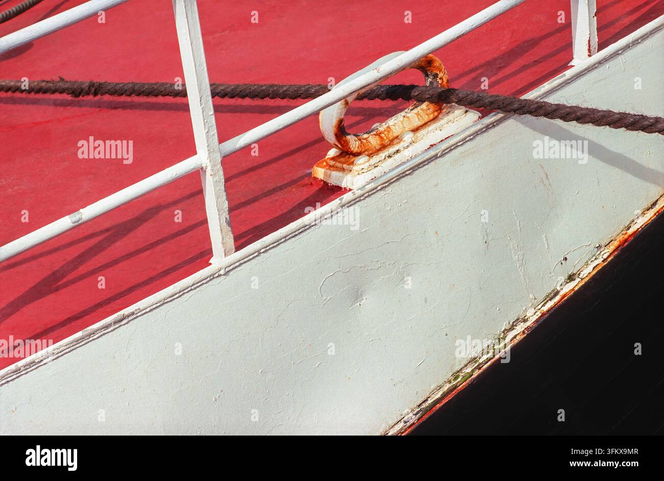 Détail d'une taquet rouillée et d'une corde enroulée sur le pont rouge patiné d'un bateau montrant des signes de vieillissement Banque D'Images