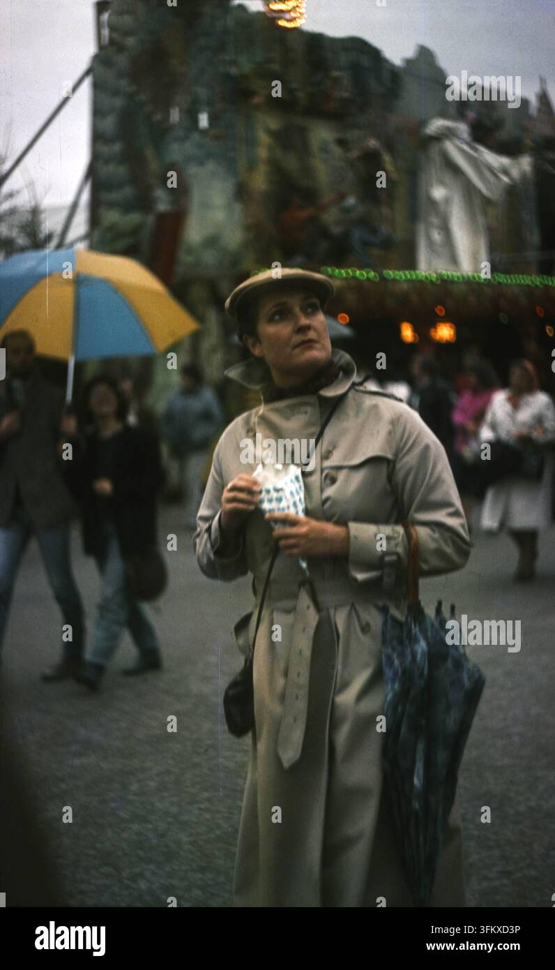 Munich, Allemagne de l'Ouest - 1er octobre 1984 : femme en trench-coat tenant des bonbons à l'Oktoberfest Banque D'Images