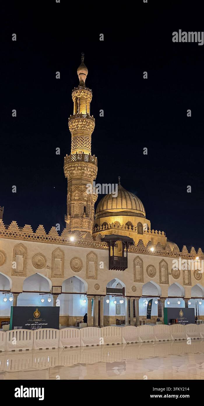 Mosquée Al-Azhar illuminée la nuit, présentant son minaret orné, son dôme et sa cour historique au Caire, en Égypte. - Image de stock capturée avec un smartphone
