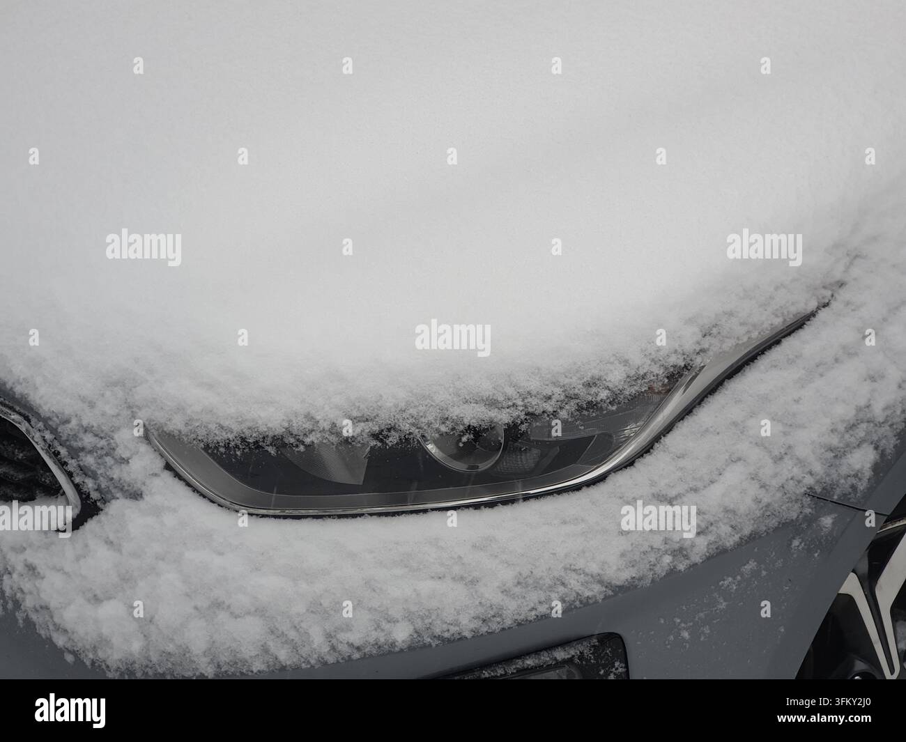 Vue rapprochée du phare d'une voiture moderne et du capot avant recouvert d'une épaisse couche de neige blanche fraîche. Le véhicule semble être garé à l'extérieur Banque D'Images