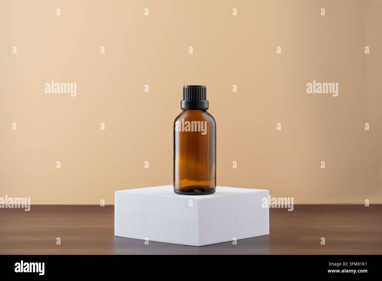 Flacon en verre ambré de 50 ml pour huile essentielle sur un podium carré blanc, fond beige Banque D'Images