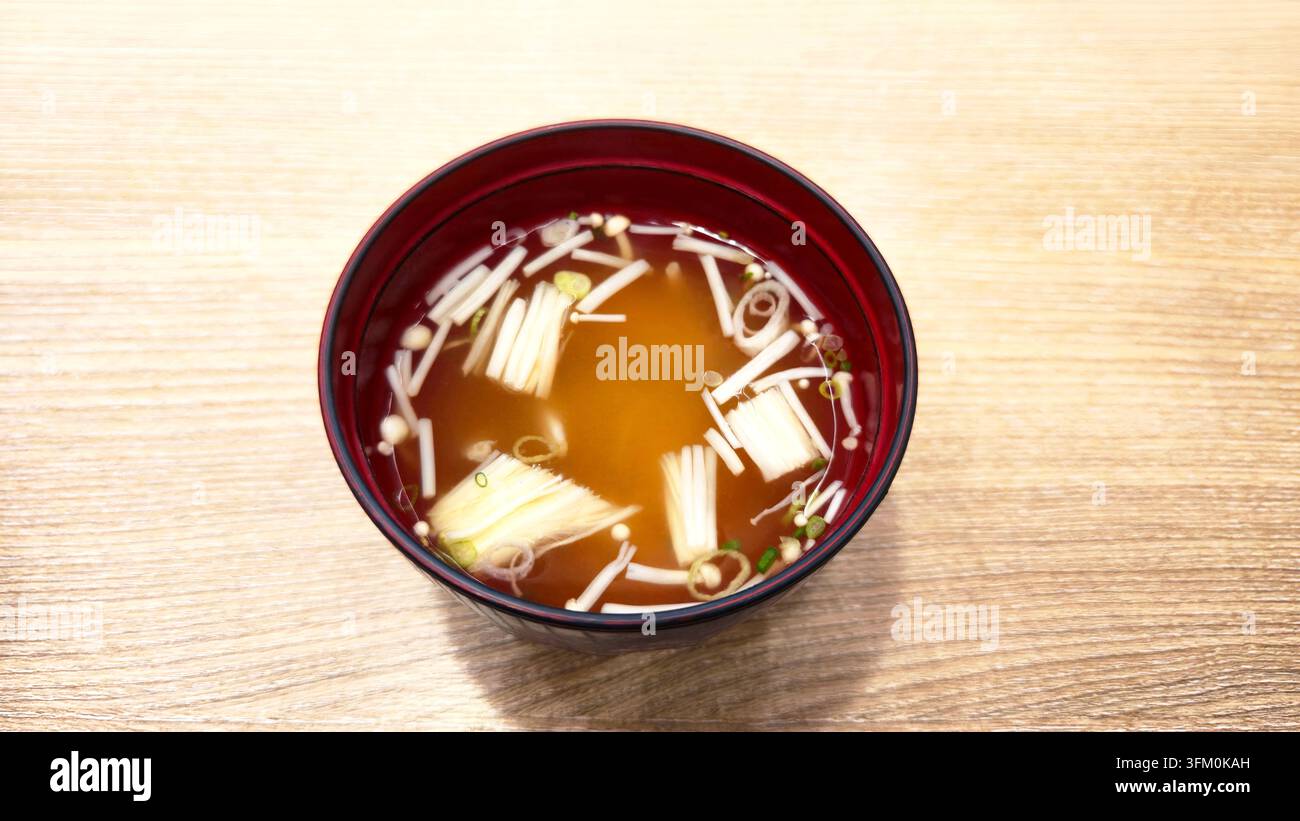 Soupe claire japonaise traditionnelle aux champignons enoki et oignons verts servie dans un bol en laque rouge sur une table en bois avec espace pour du texte. - Image de stock capturée avec un smartphone