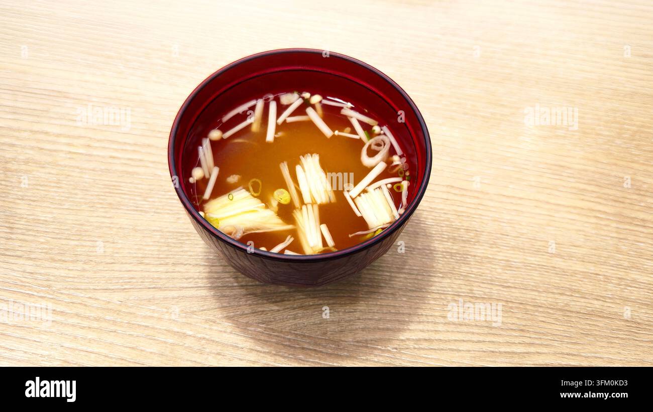 Soupe claire japonaise traditionnelle aux champignons enoki et oignons verts servie dans un bol en laque rouge sur une table en bois avec espace pour du texte. - Image de stock capturée avec un smartphone