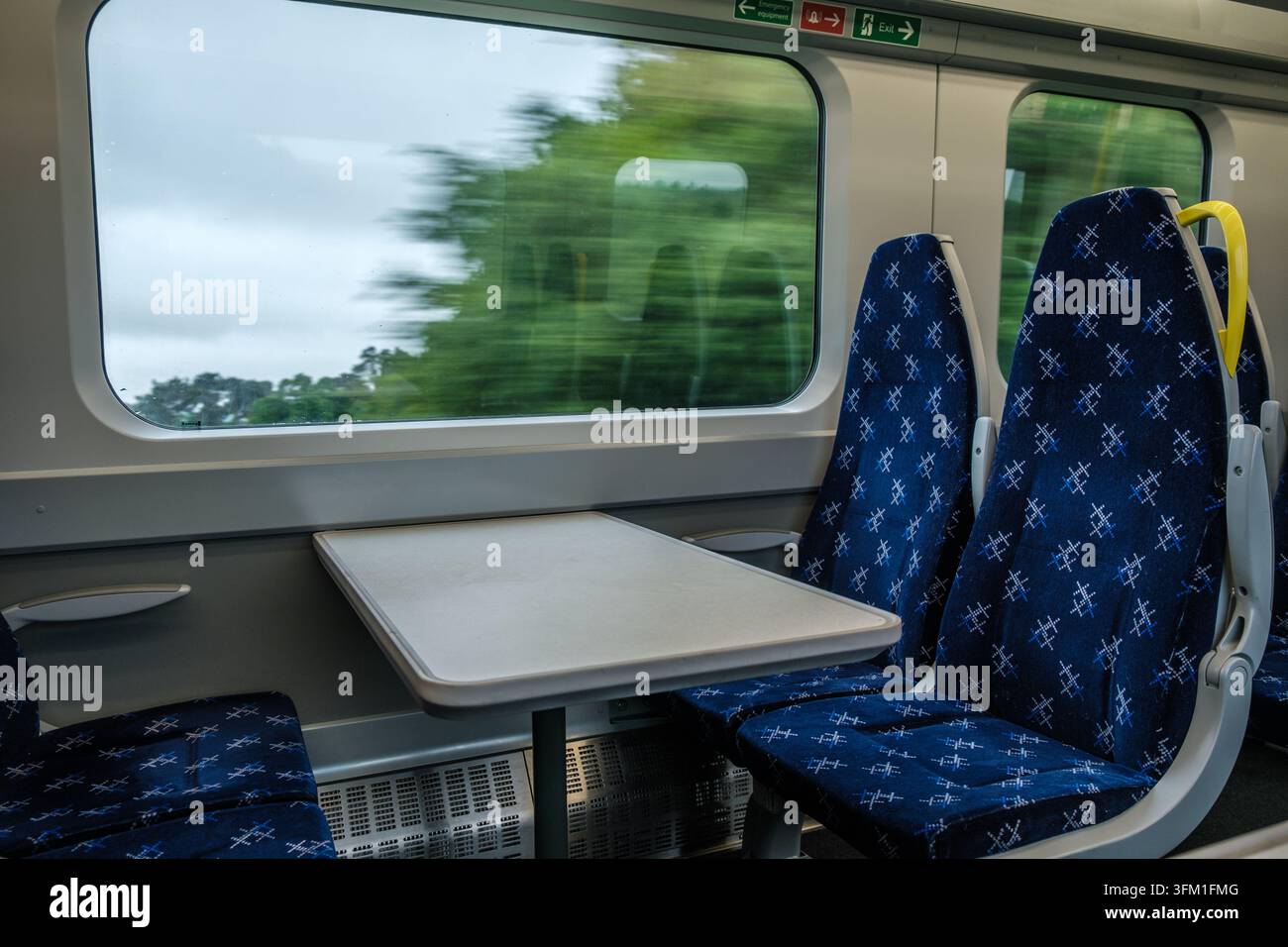 Sièges vides et table à l'intérieur du wagon du train avec flou de mouvement à l'extérieur de la vitre Banque D'Images