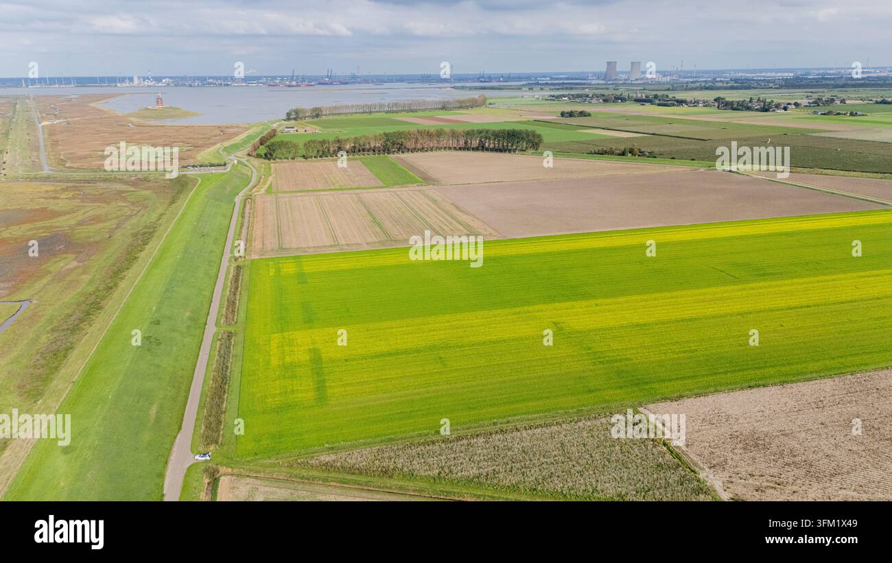 Vue aérienne montrant les tours de la centrale nucléaire de Doel et la zone portuaire industrialisée contrastant avec les champs agricoles et les zones humides Banque D'Images