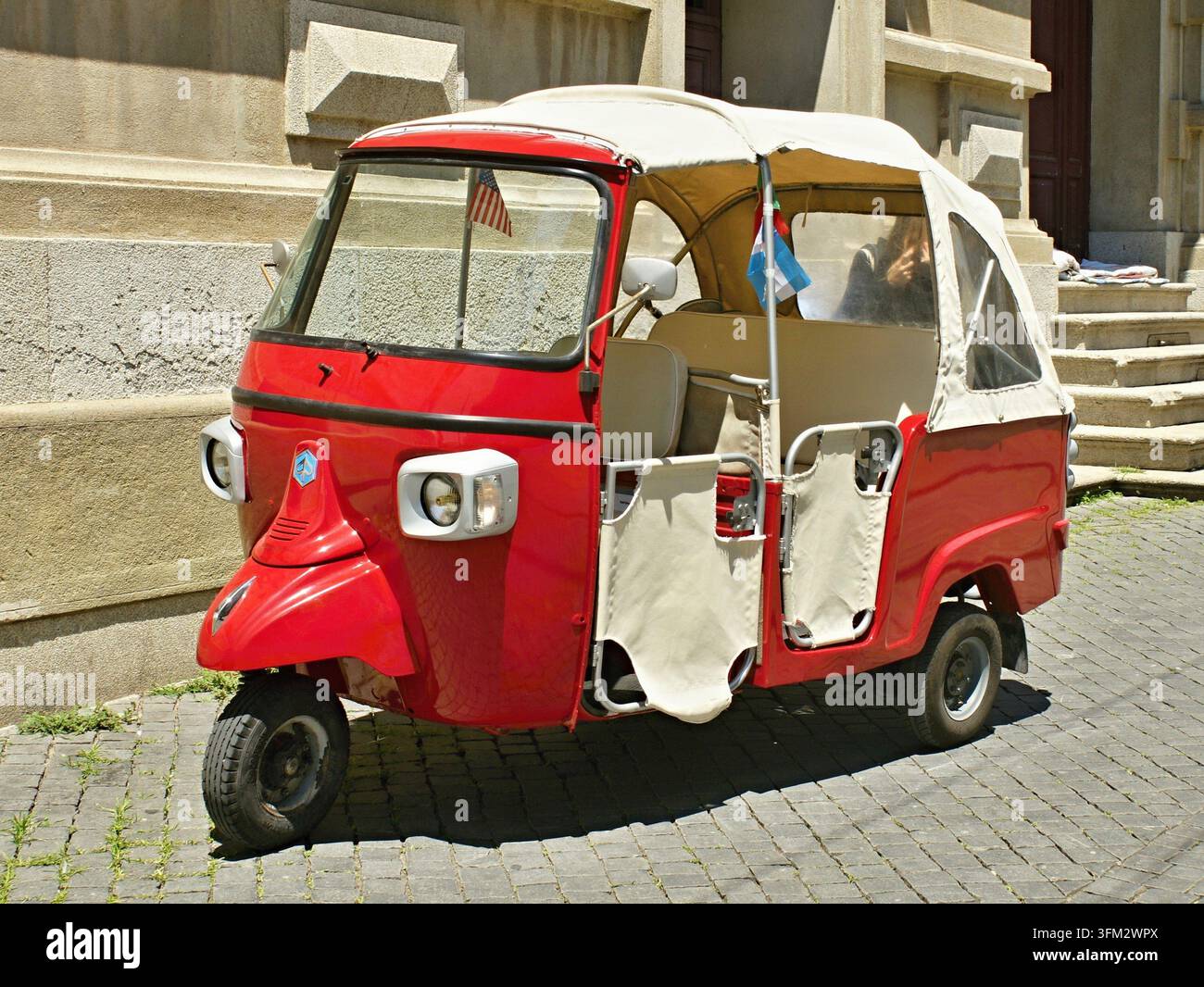 Tricycle Auto-rickshaw Piaggio Ape rouge garé sur une rue pavée ensoleillée Banque D'Images
