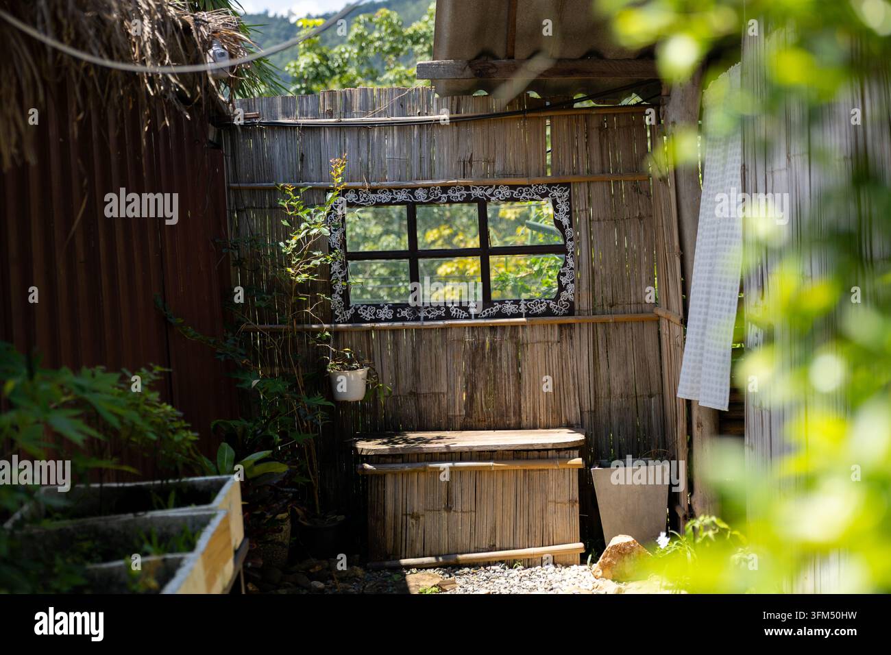 Un abri de jardin en bambou avec fenêtre, comptoir en bois et feuillage luxuriant créant une retraite extérieure paisible Banque D'Images