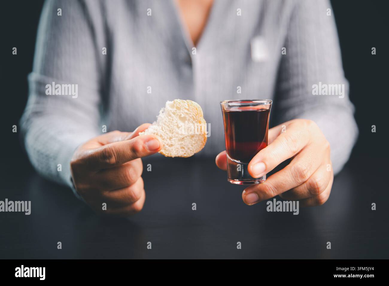 Person tenant du pain et un petit verre de boisson de communion rouge foncé, illustrant un moment de culte chrétien significatif de foi, de prière, de souvenir sacré Banque D'Images