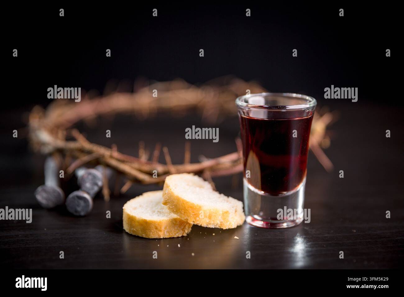 Boisson rouge foncé et pain tranché à côté d'une couronne d'épines et de clous métalliques sur une table noire, créant un nature mort solennel de communion chrétienne pour la foi Banque D'Images