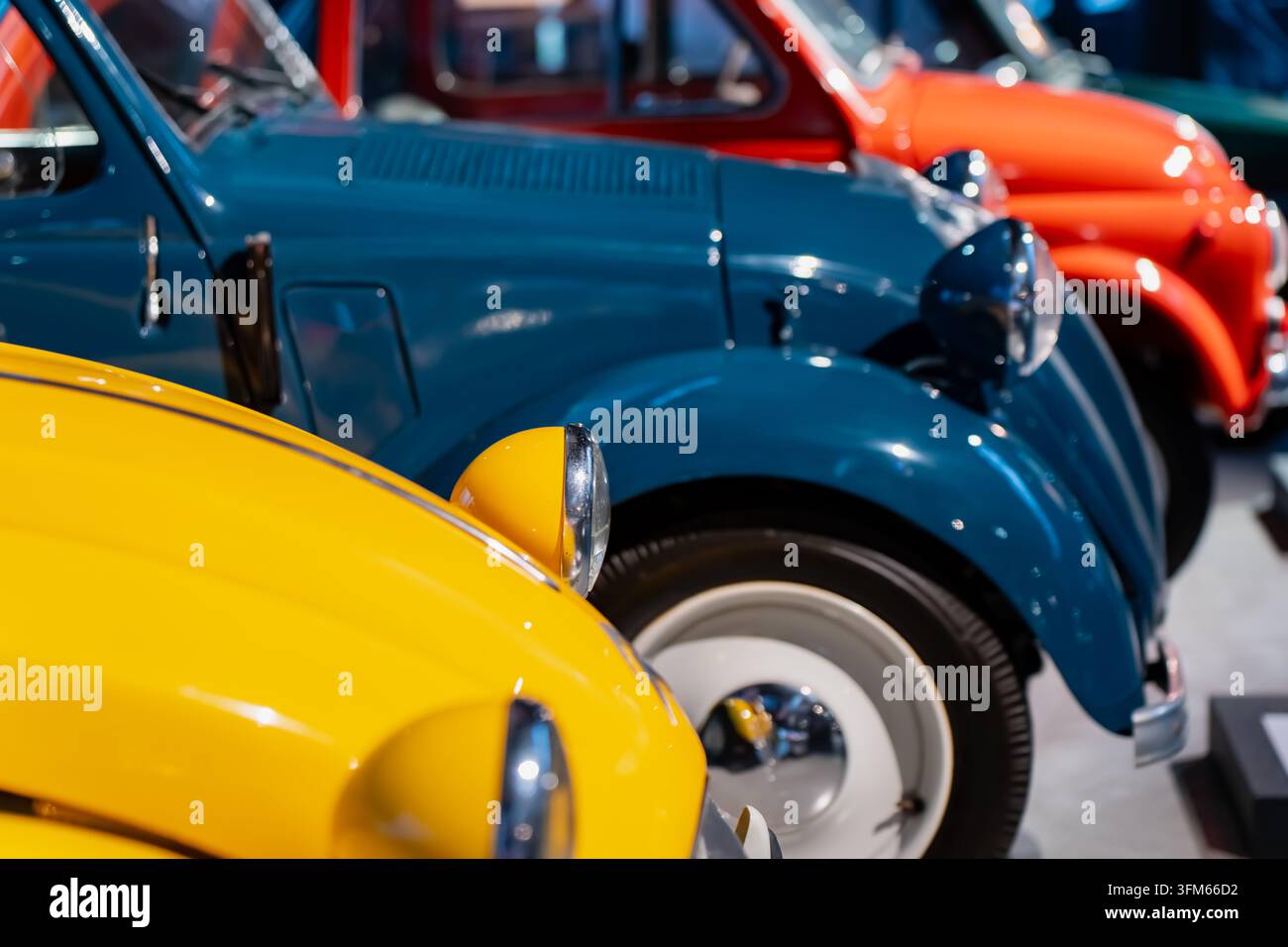 Voitures de collection aux couleurs vives avec des panneaux bleus, jaunes, orange et rouges dans un musée, soutenant les expositions automobiles, la recherche en restauration et les collaborations Banque D'Images