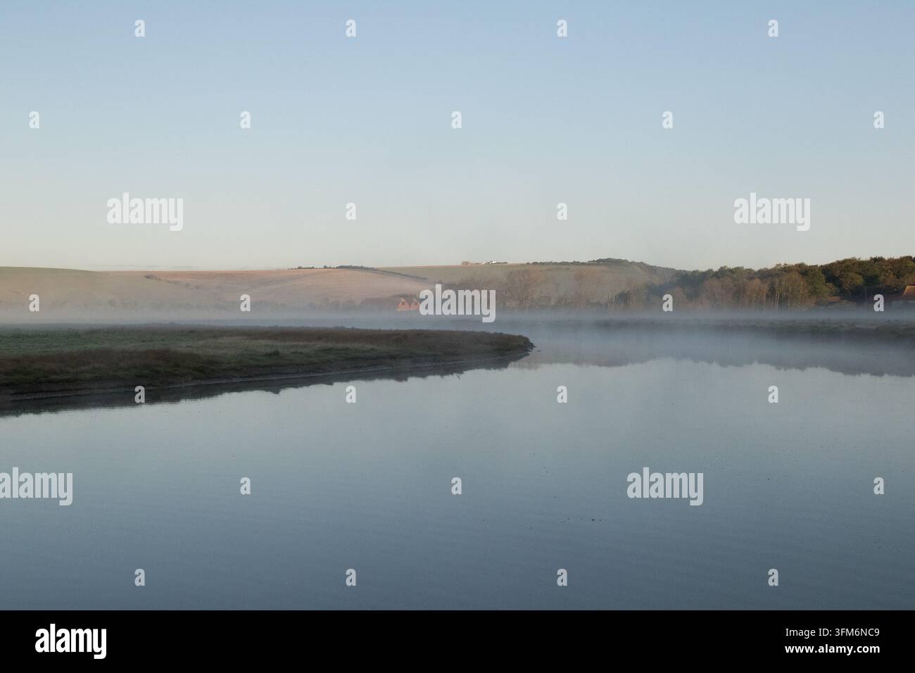 Brume matinale tranquille s'élevant au-dessus de la rivière Cuckmere avec des reflets d'eau immobile et les collines verdoyantes de Sussex ondulant à l'horizon. Banque D'Images